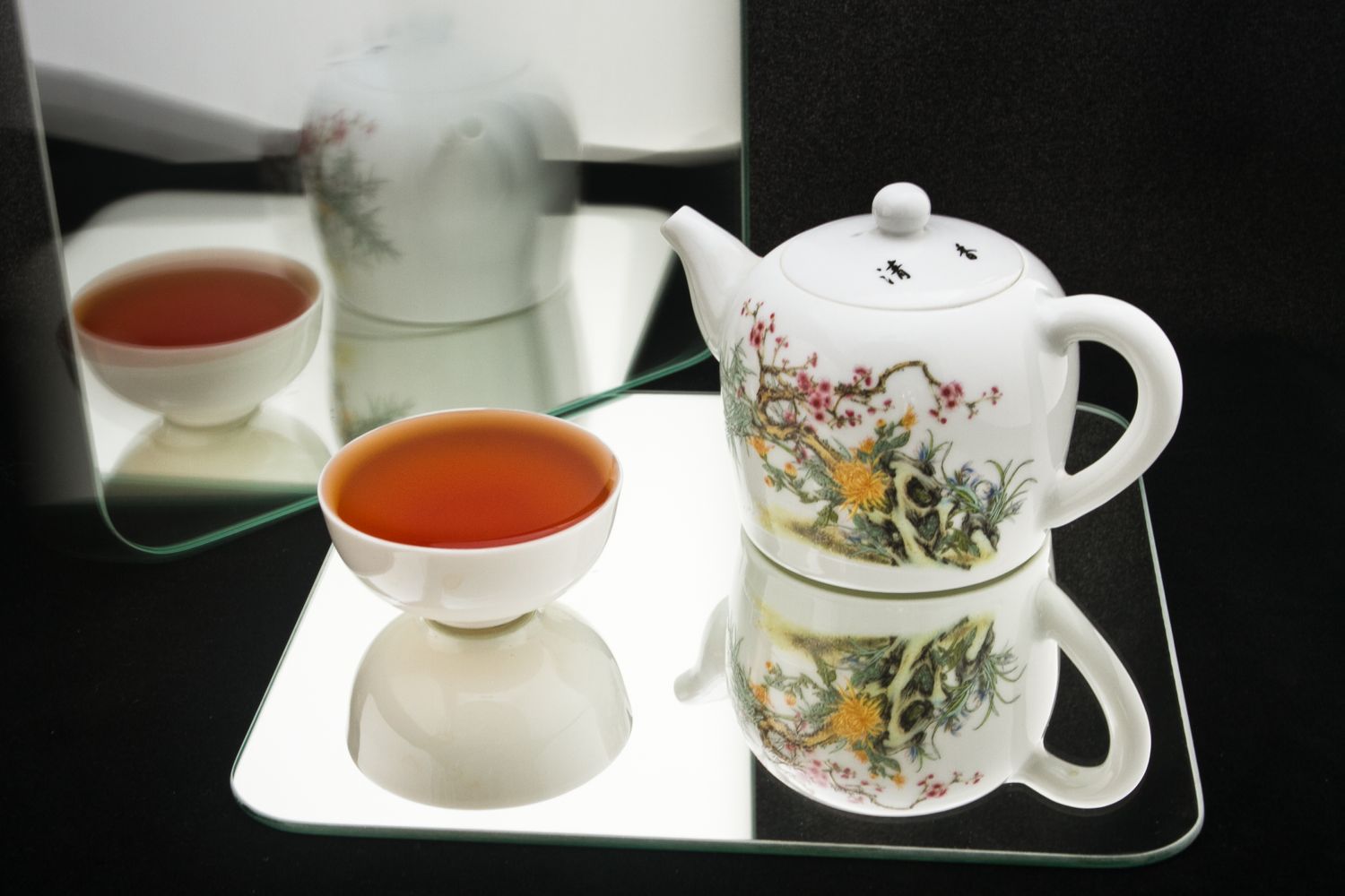 Black tea and traditional chinese white porcelain tea cup and teapot with mirror reflections