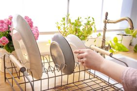 A person placing dishes on a drying rack in a kitchen