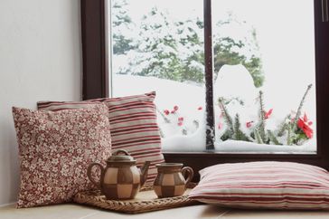 Tea set and pillows on window seat with snow outside