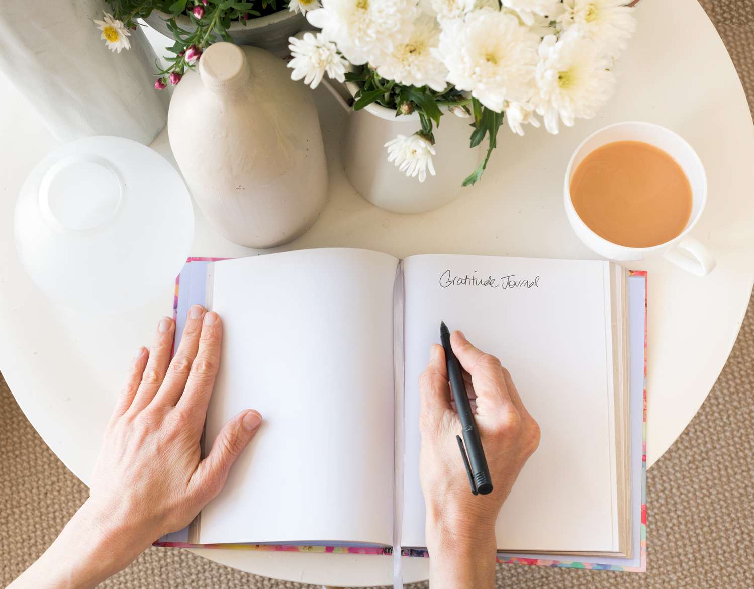 hands writing in journal on table with coffee cup and flowers