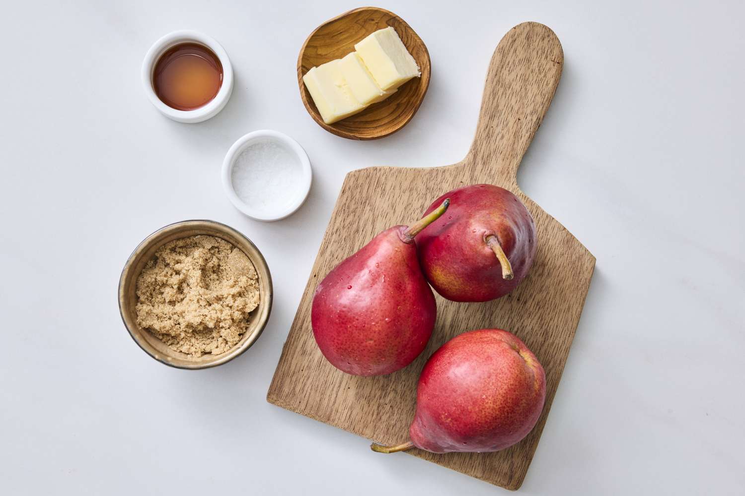 Ingredients for caramelized pears including red pears butter brown sugar and small containers of salt and liquid flavoring