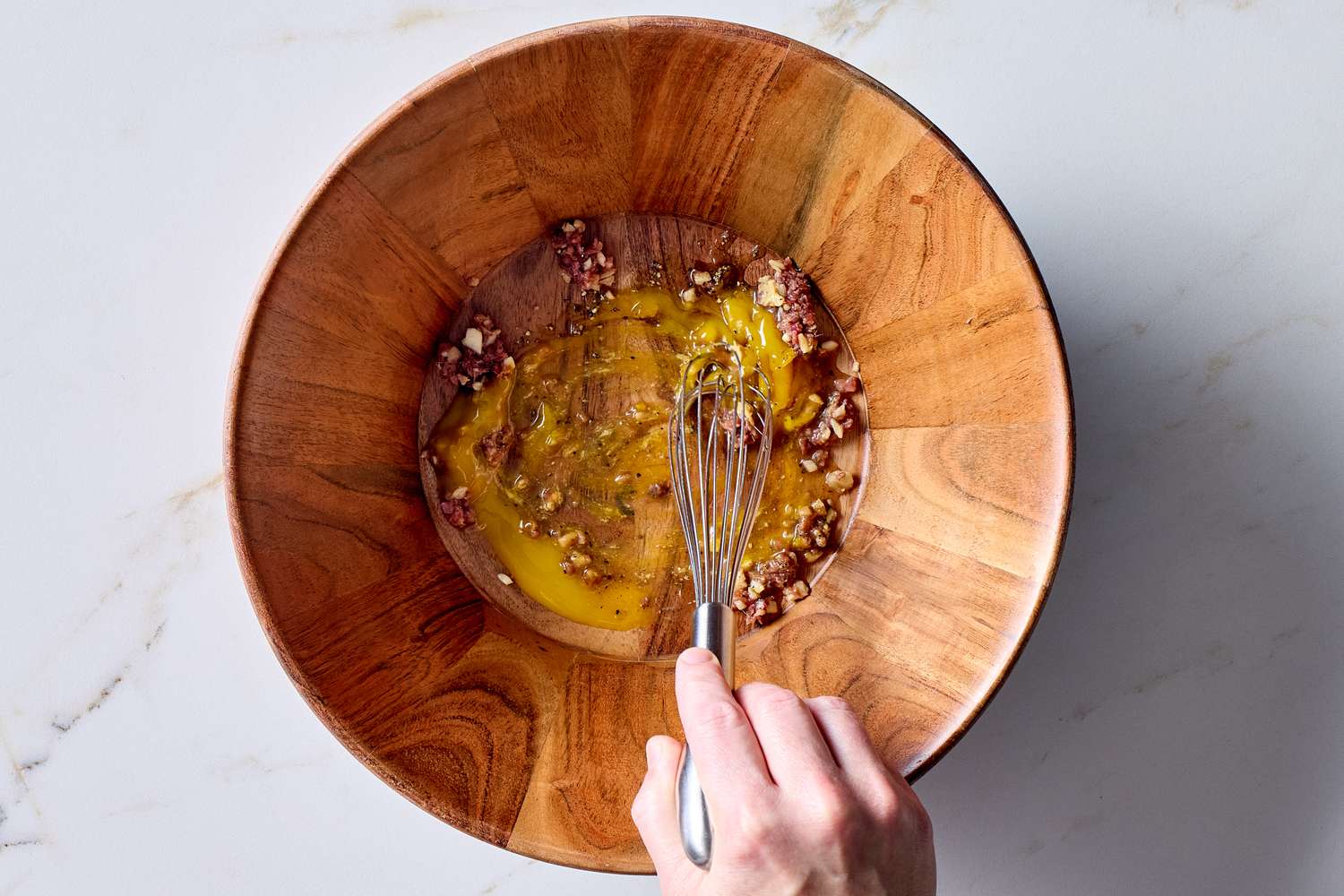 Whisking ingredients in a wooden bowl preparing Caesar salad dressing