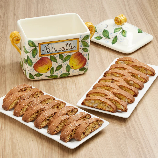 A decorative ceramic biscotti jar and two plates of biscotti slices on a wooden surface