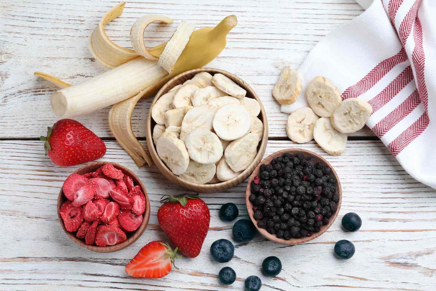 Assorted fresh and freezedried fruits including strawberries blueberries and bananas on a wooden surface