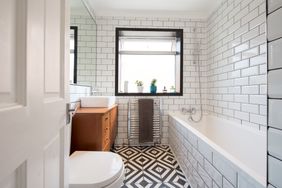 Modern bathroom with a bathtub white subway tiles geometric floor tiles wood vanity and a central window with plants on the sill