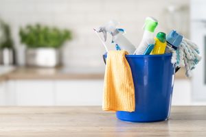 Cleaning supplies in a blue bucket on a kitchen counter including bottles a cloth and a mop