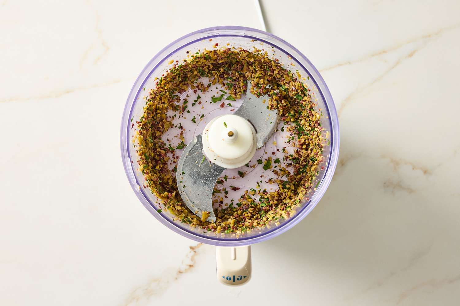 A food processor filled with a chopped seasoning mixture viewed from above