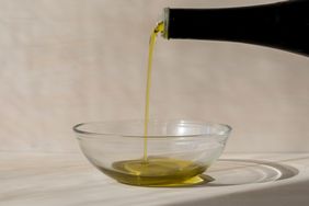 Olive oil being poured into a glass bowl from a bottle
