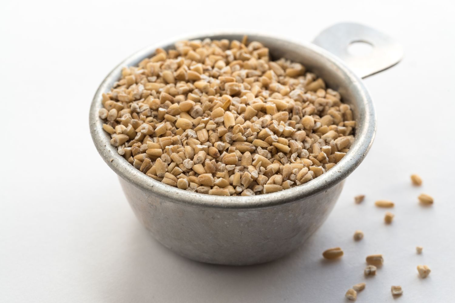 Small steel cup filled with uncooked steelcut oats isolated on a white surface