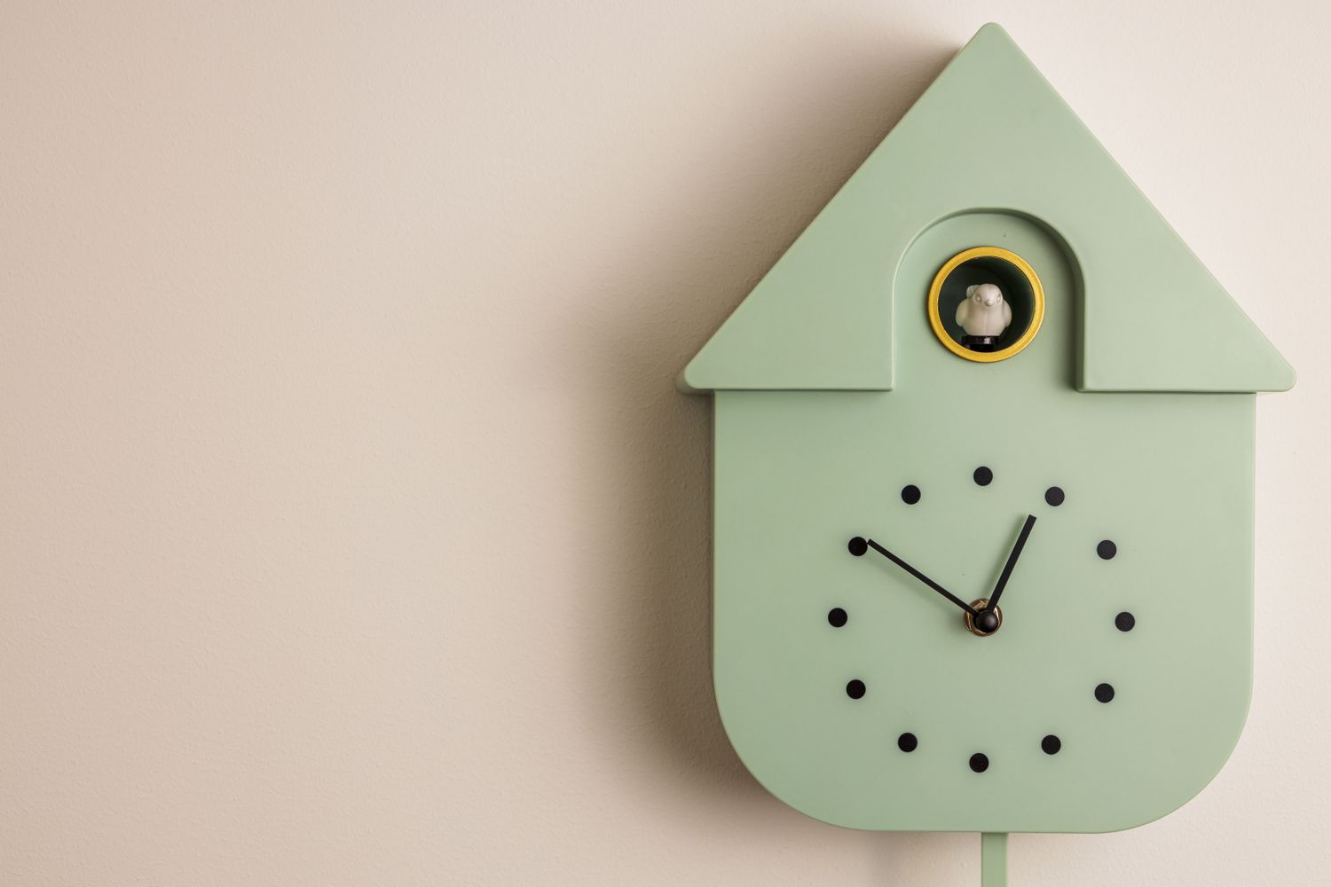 A minimalist wall clock shaped like a house with a cuckoo bird feature displayed in a small circular window