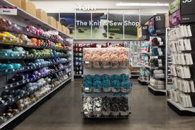 A craft store aisle featuring yarn displays organized shelves of acrylic and fabric sections visible
