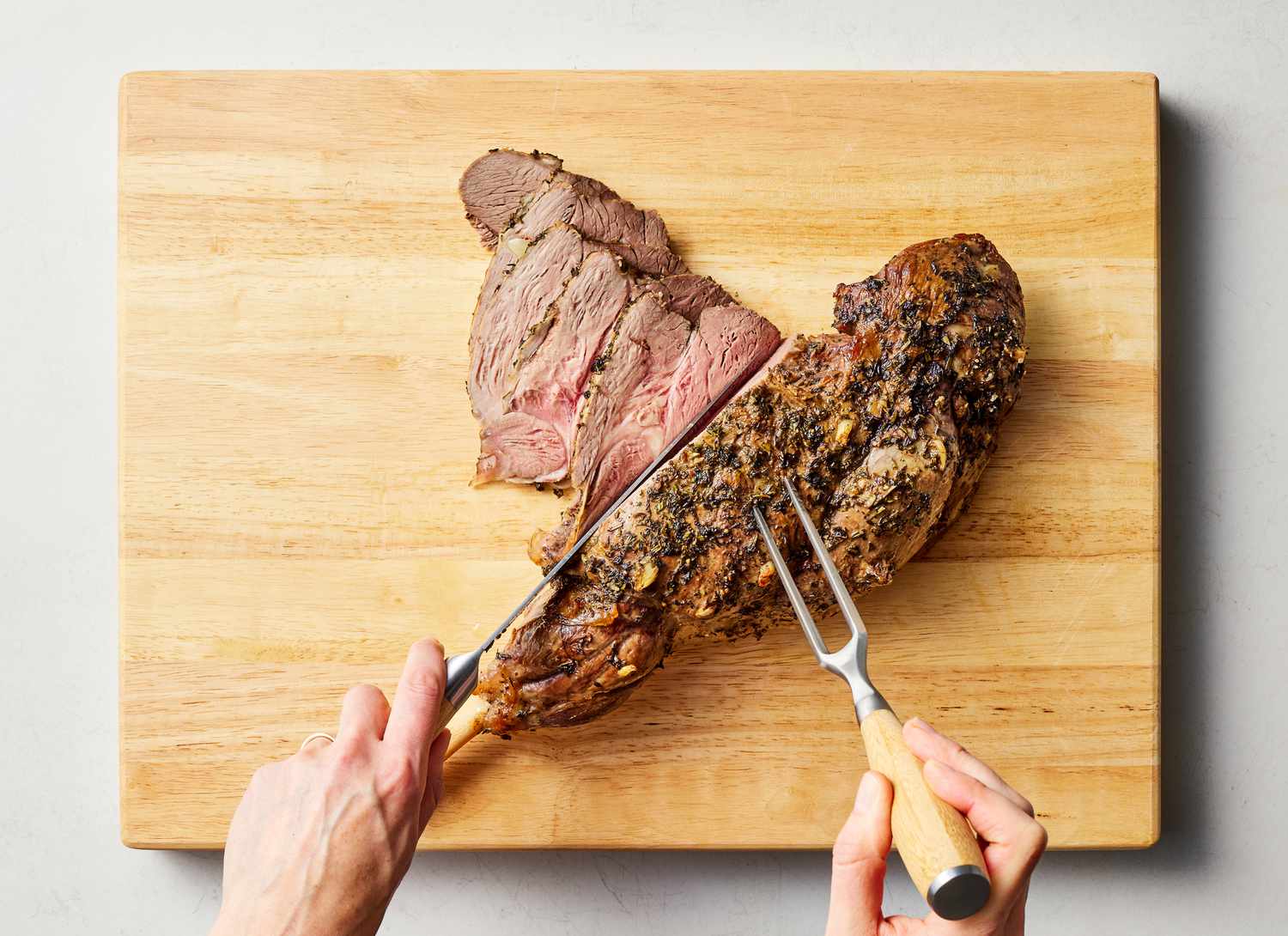 someone carving roast lamb on a cutting board