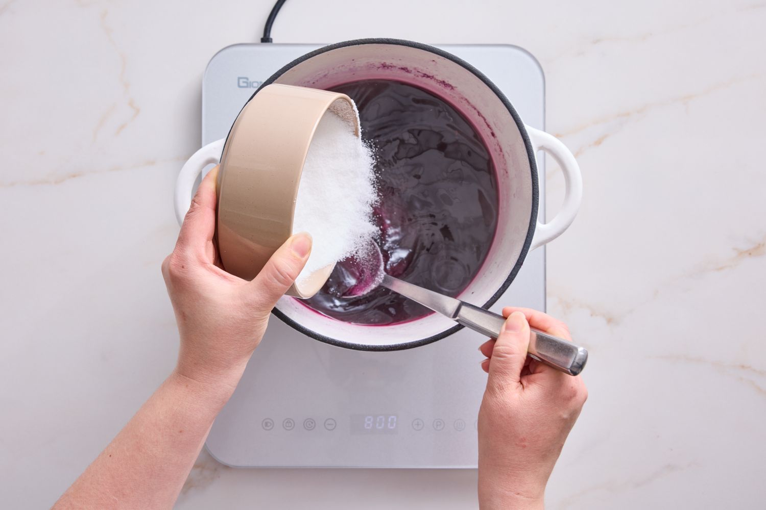 Hands adding an ingredient into a pot on a stovetop