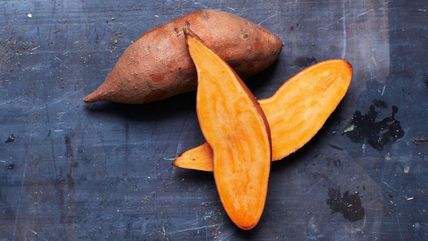 sweet potatoes, one sliced in half and one whole on dark surface