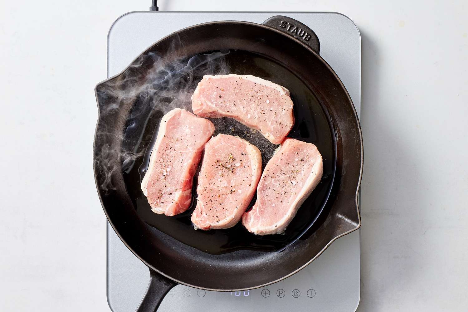 Four seasoned boneless pork chops cooking in a cast iron skillet on a stove