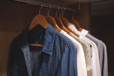 Clothing hanging on wooden hangers on a rail including a denim shirt and sweaters