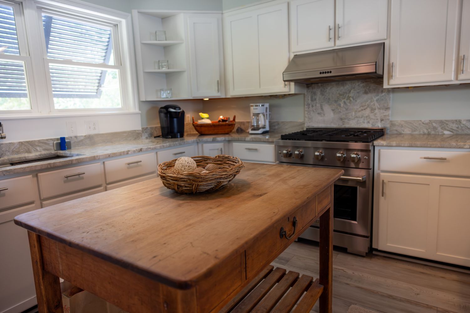 A home kitchen with wooden center table modern stove and white cabinetry
