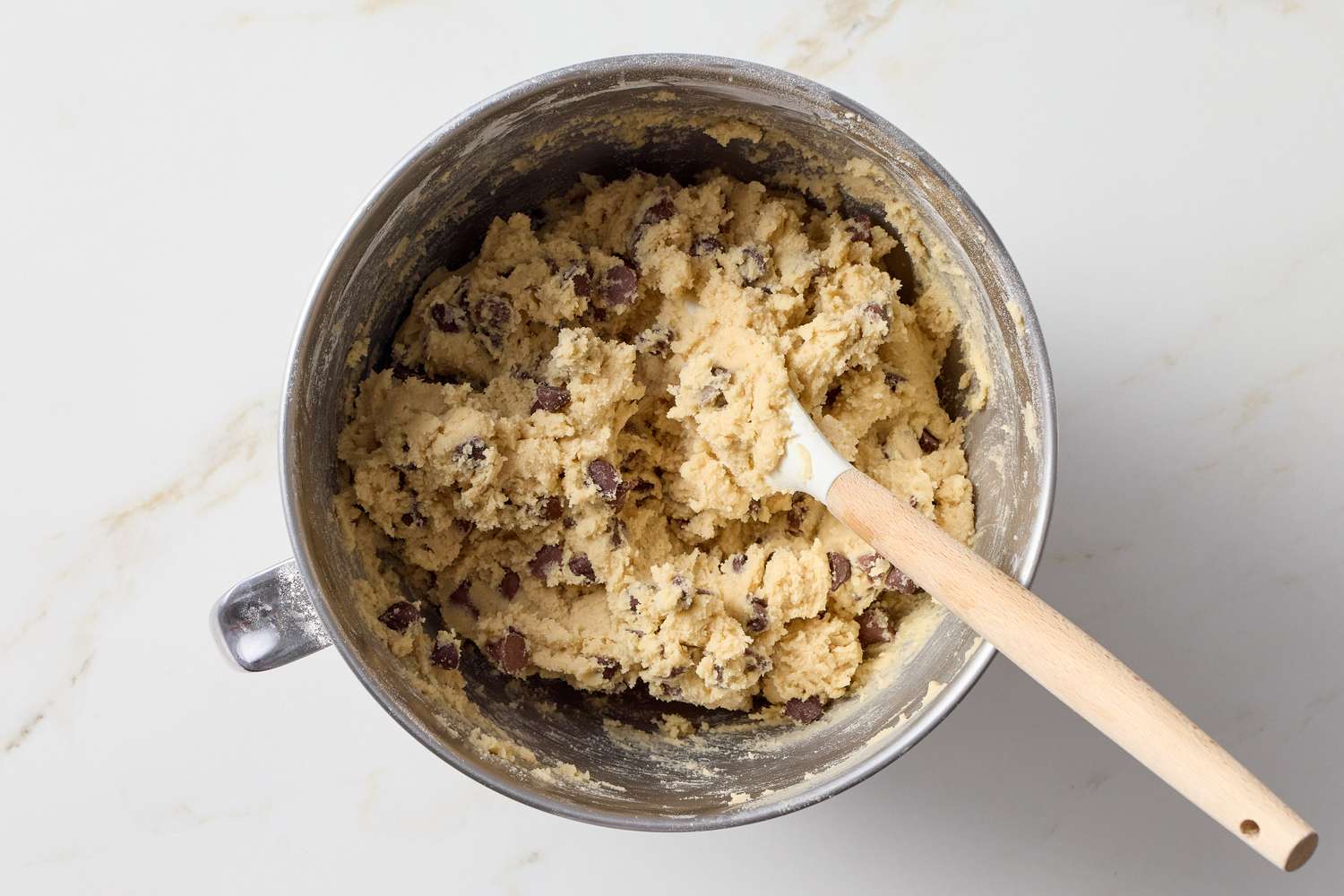 A mixing bowl containing cookie dough with a spatula