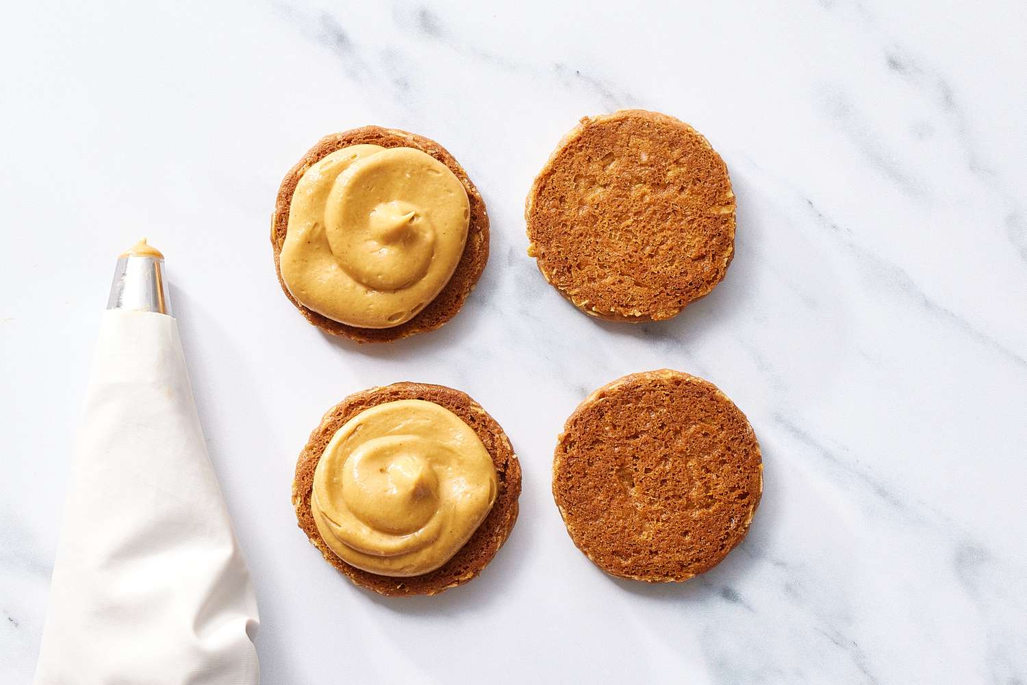 Piping bag with peanut butter filling on peanut butter sandwich cookies