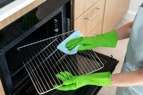 A person wearing green gloves cleaning an oven rack with a blue cloth