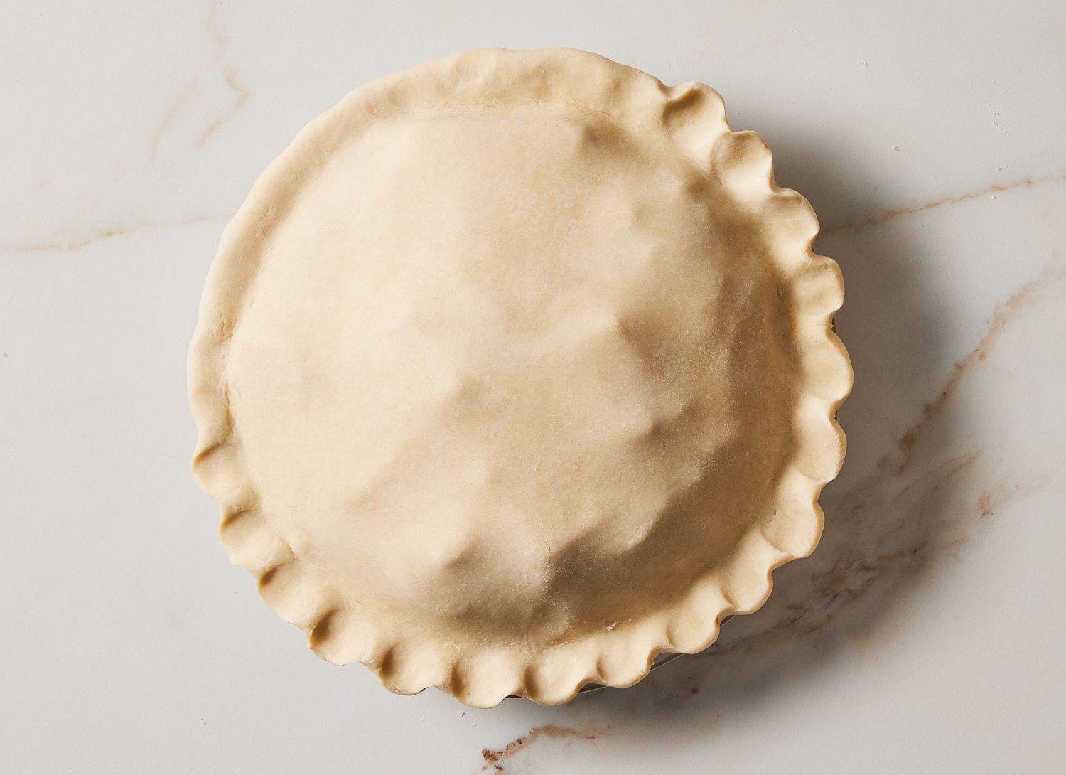 partially pinched three quarters the way around raw pie crust on a marble surface