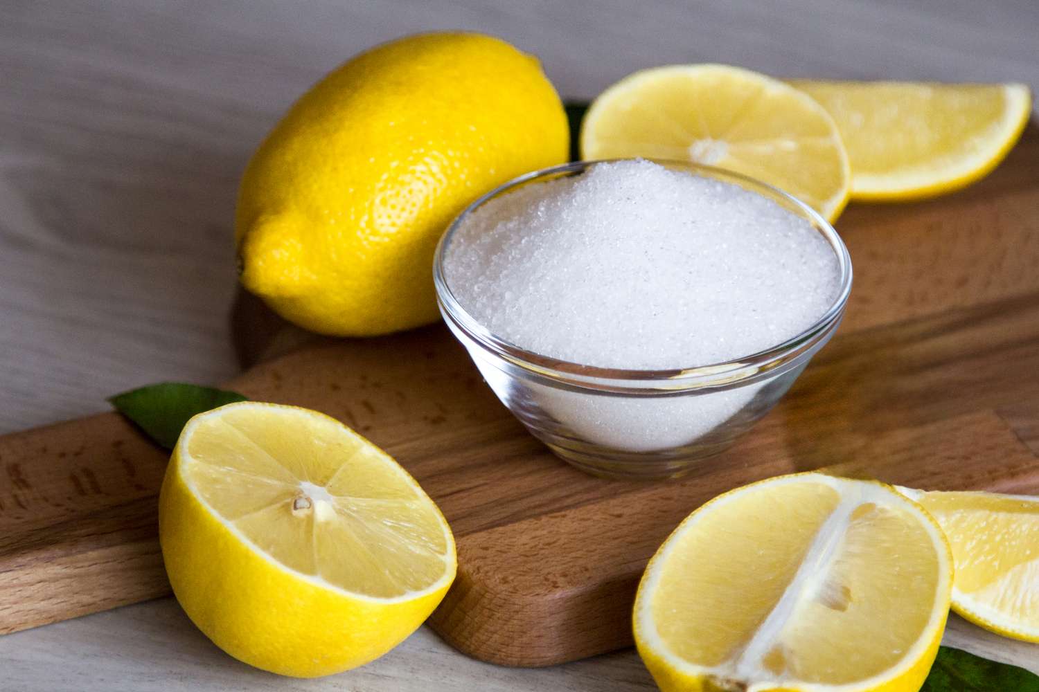 Lemons and a small bowl of granulated sugar on a wooden board