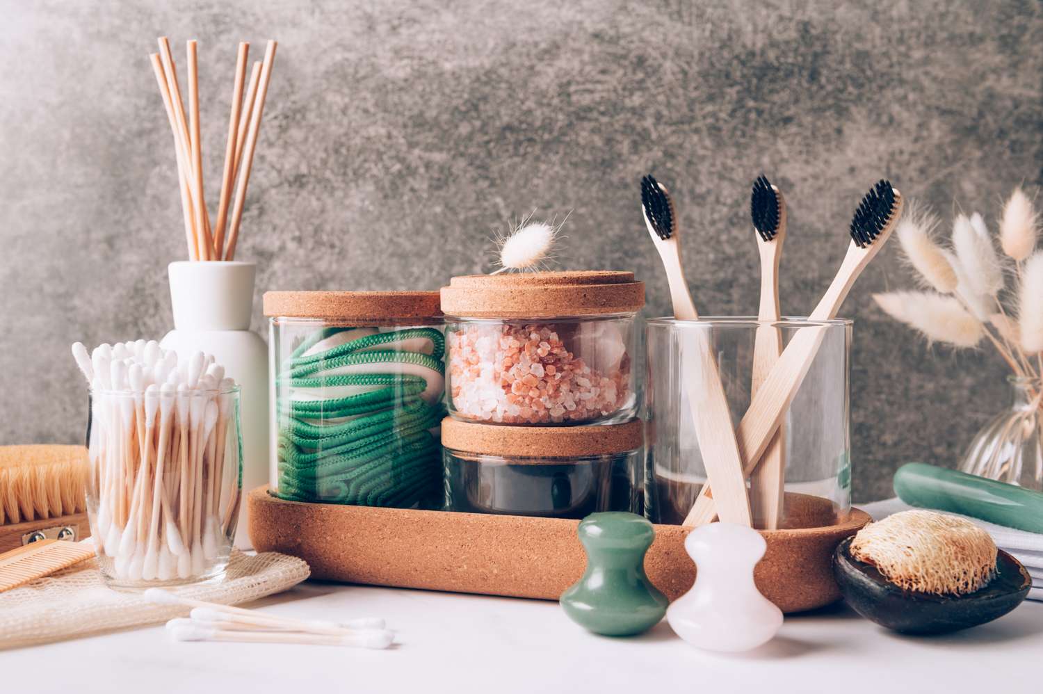 bathroom counter with bath salts, reusable cotton pads, diffuser, bamboo toothbrush, jade rollers, natural wooden brush, fresh soap, and charcoal powder