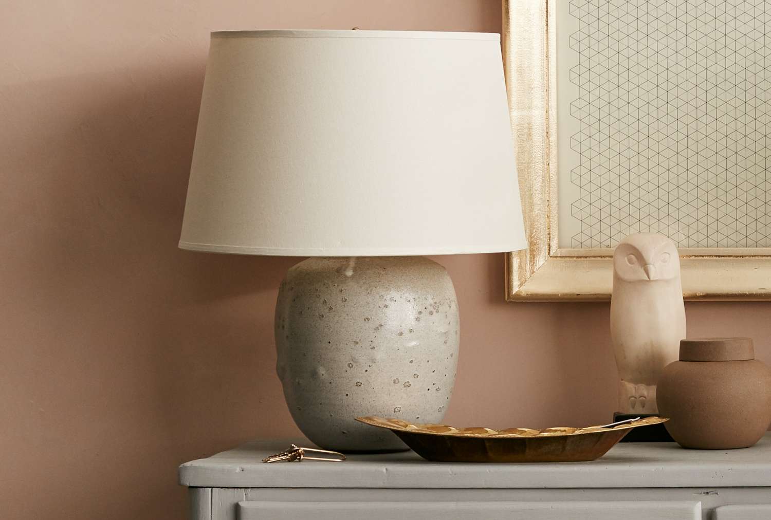 A table lamp on a sideboard with decorative items and a framed artwork on the wall