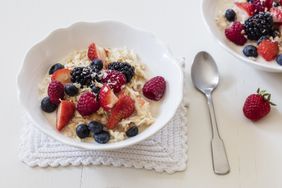 A bowl of oatmeal topped with berries and coconut with a spoon nearby on a textured mat