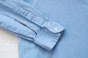 A blue shirt with a black sharpie stain on the sleeve showing closeup of the buttons and the mark