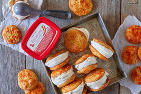 Ice cream sandwiches made with biscuits and a tub of ice cream on a wooden surface