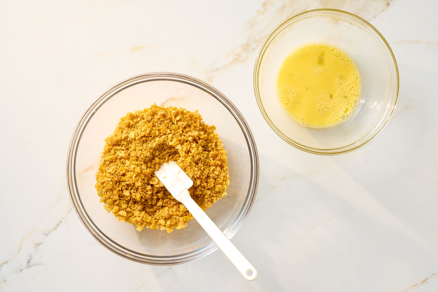 Two bowls one with crushed cornflakes and a spatula the other with beaten eggs