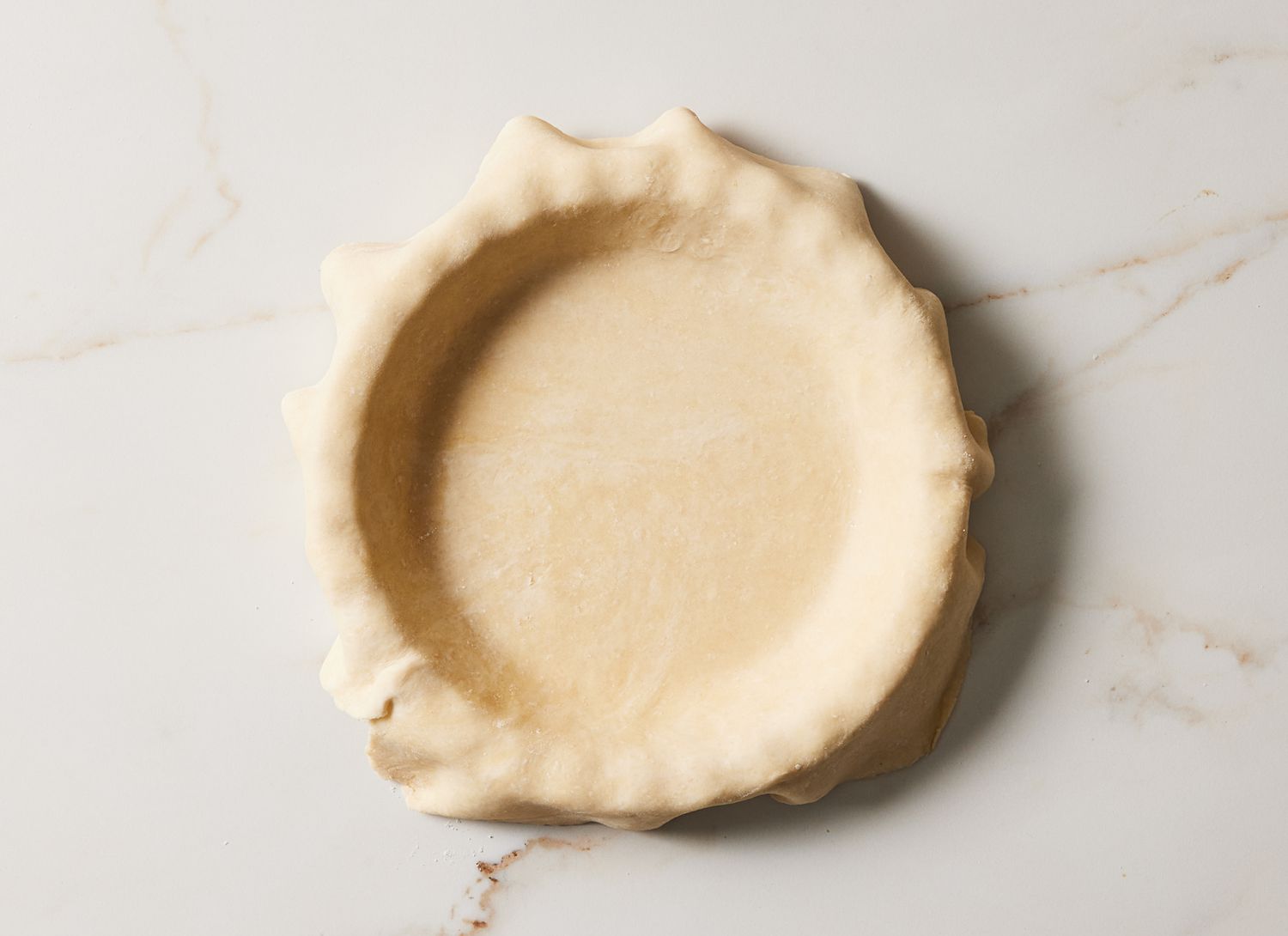 overhead view of pie dough in a pie pan on marble surface