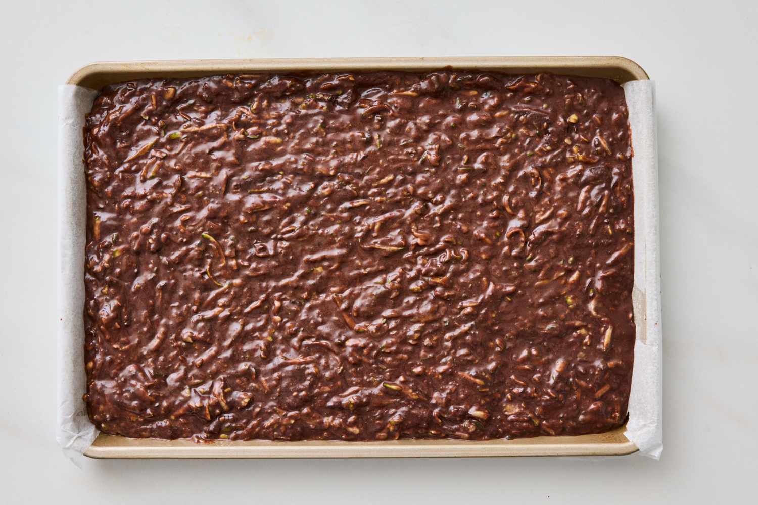 Unbaked chocolate zucchini cake batter spread evenly in a rectangular baking pan lined with parchment paper