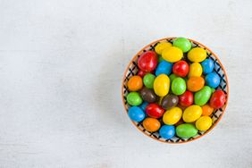 A bowl filled with colorful candycoated chocolates on a light surface