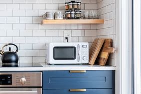 A white microwave placed on a kitchen countertop beneath a shelf with spices