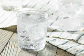 A glass of carbonated water with ice cubes placed on a wooden surface with a striped cloth