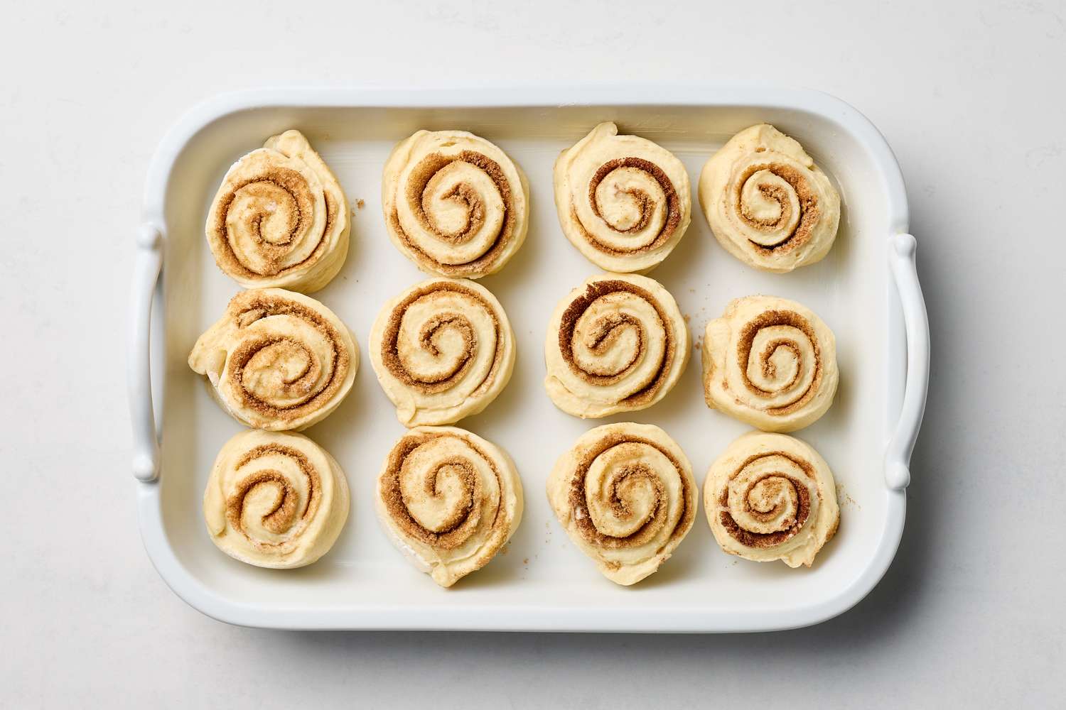 Unbaked cinnamon rolls arranged in a white baking dish