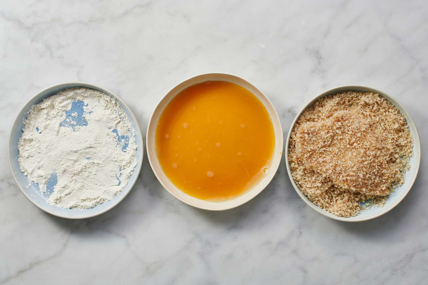 chicken breast being coated in breadcrumbs