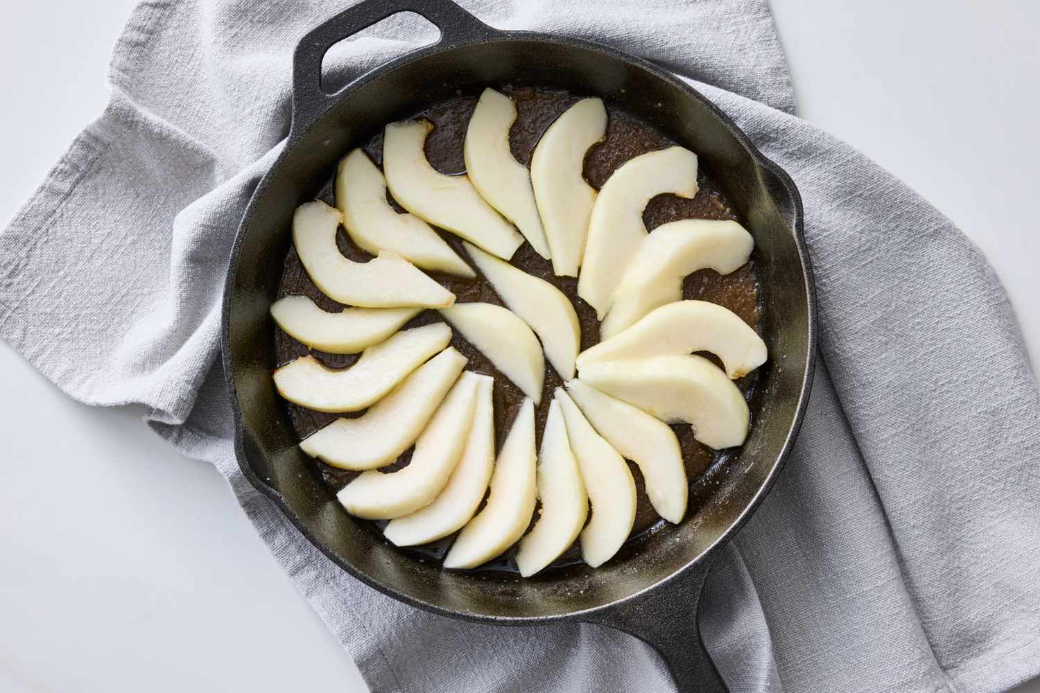 Skillet with sliced pear arranged in a circular pattern on a countertop