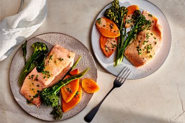 Two plates with salmon broccolini and slices of yam or carrot arranged as a meal photographed on a bright tabletop