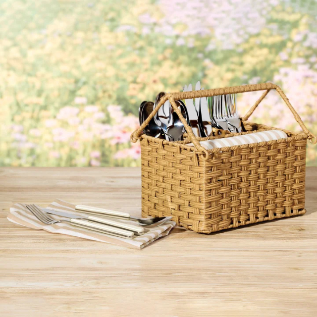 A woven basket holding utensils with additional utensils and napkins on a wooden surface