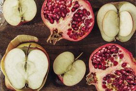 Cut halves of apples and pomegranates on a wooden surface