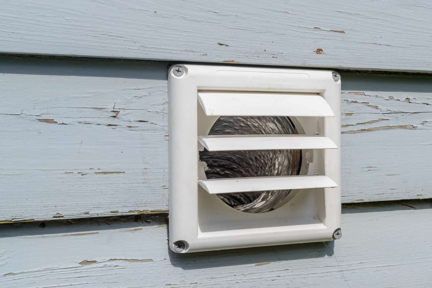 A closeup of an exterior wall dryer vent with a visible exhaust duct inside