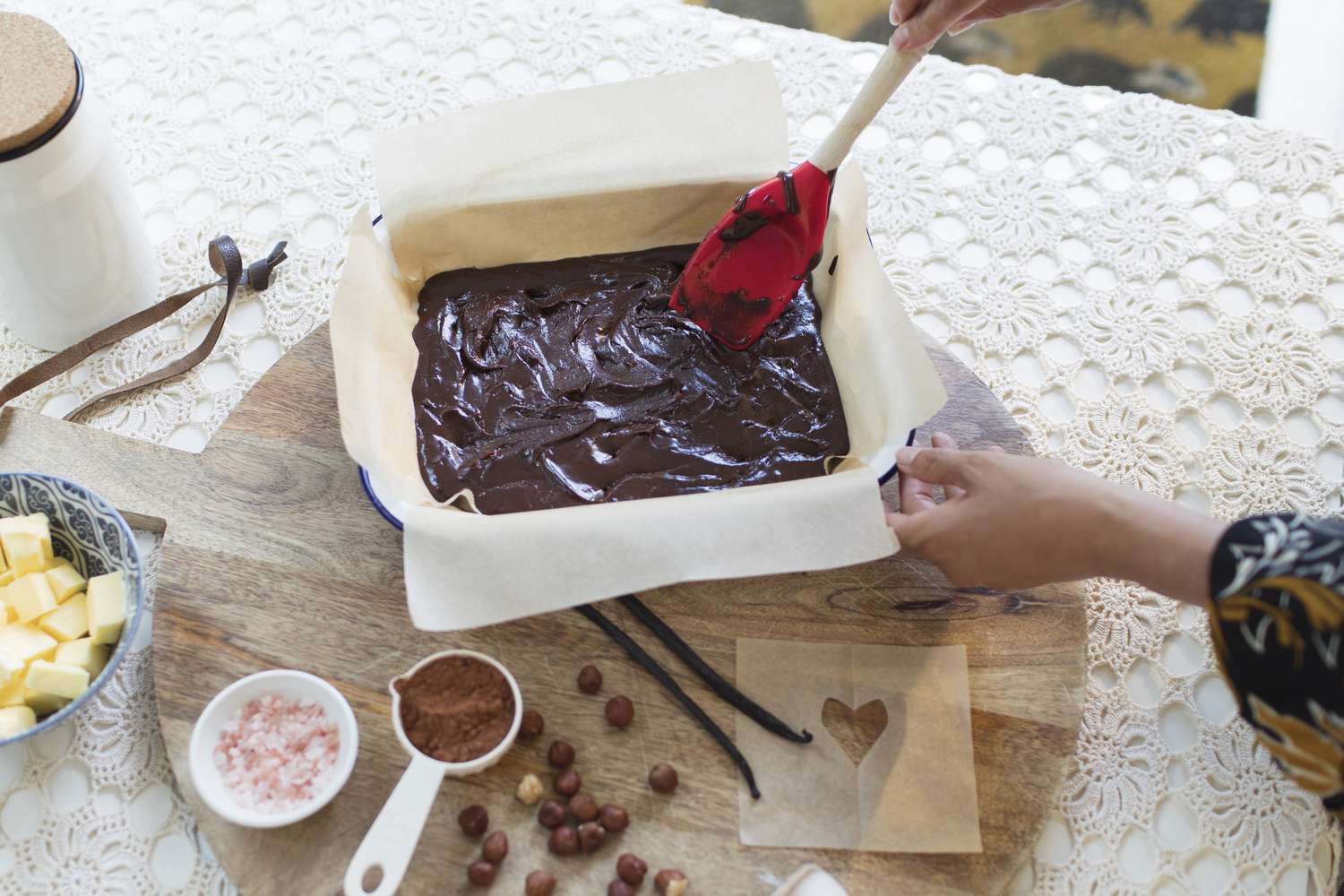 High angle view of woman baking chocolate cake at dining table, spreading batter in pan with spatula