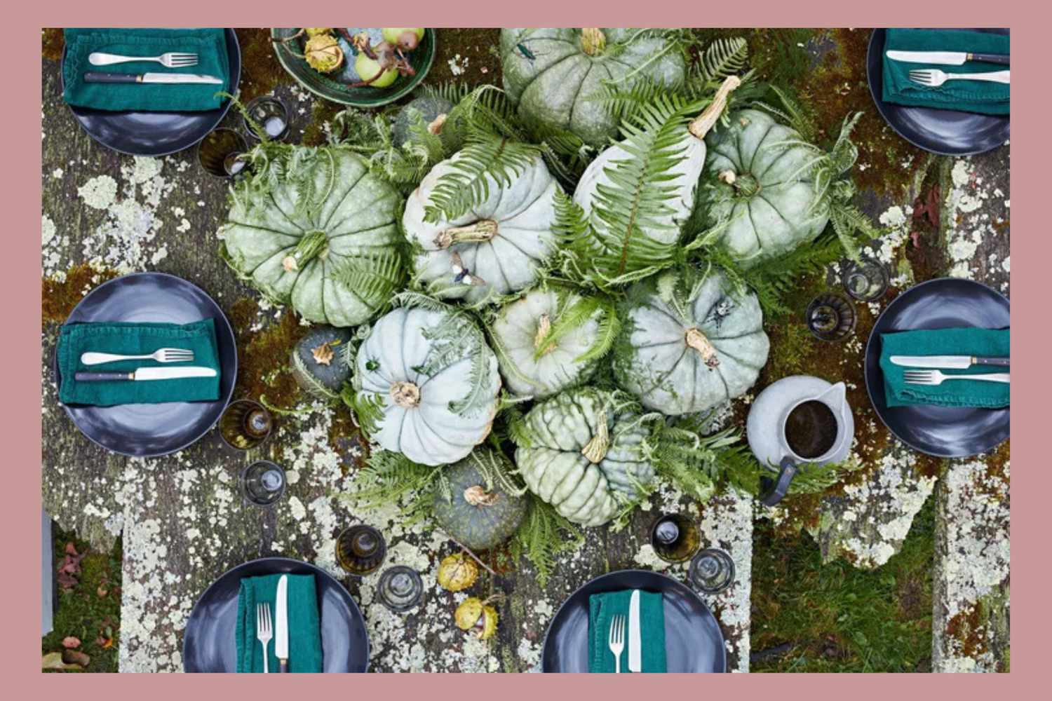 Centerpiece arrangement of pumpkins and ferns on a decorated table with set place settings