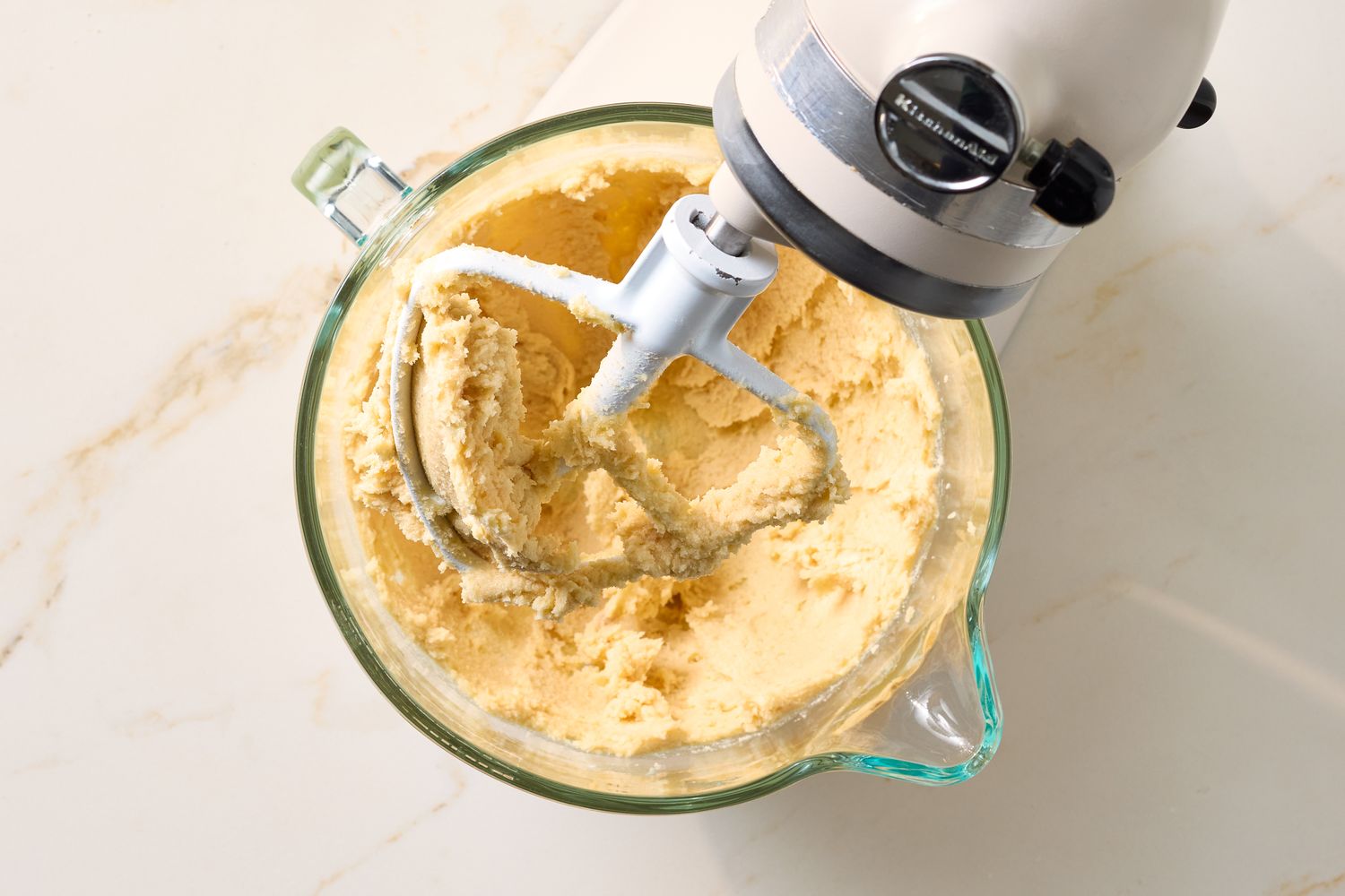A stand mixer with creamy cookie dough in a glass bowl
