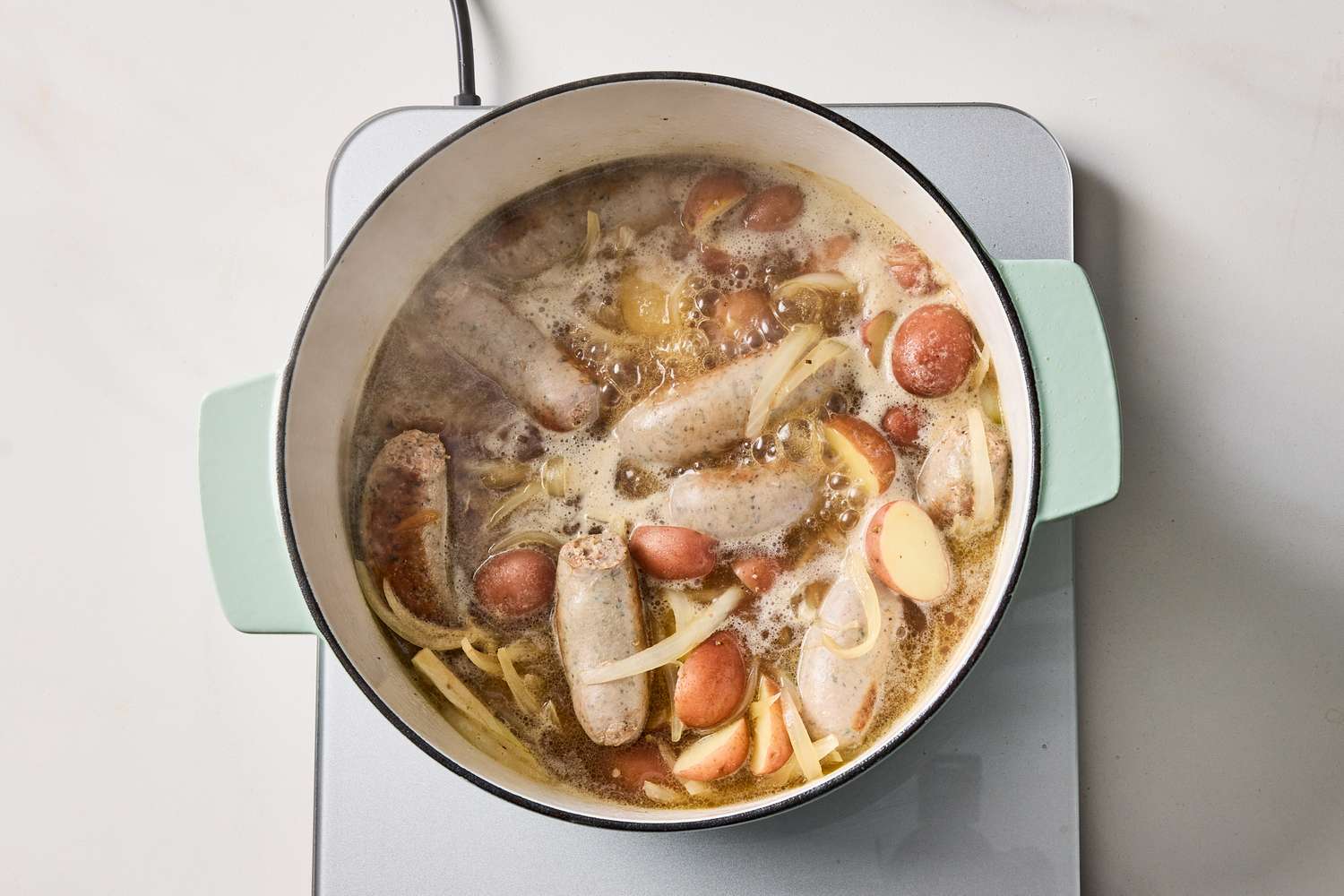 Pot of sausages and potatoes in a broth cooking on a stovetop