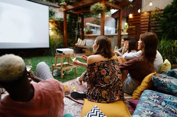 Group of people enjoying an outdoor movie screening on a patio with a projector and cushions