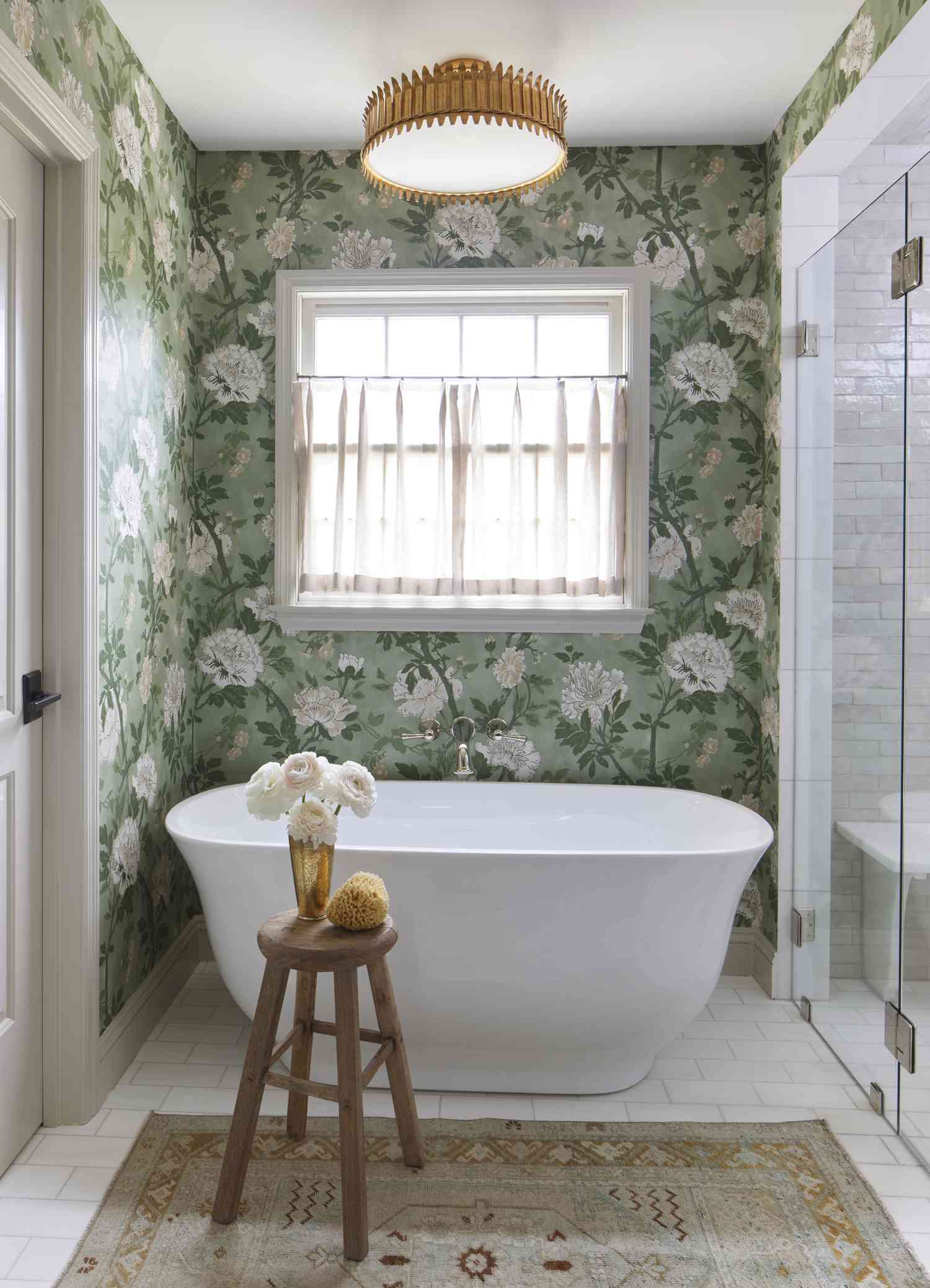 a green floral wallpaper covers a wall, bathtub and stool in the foreground